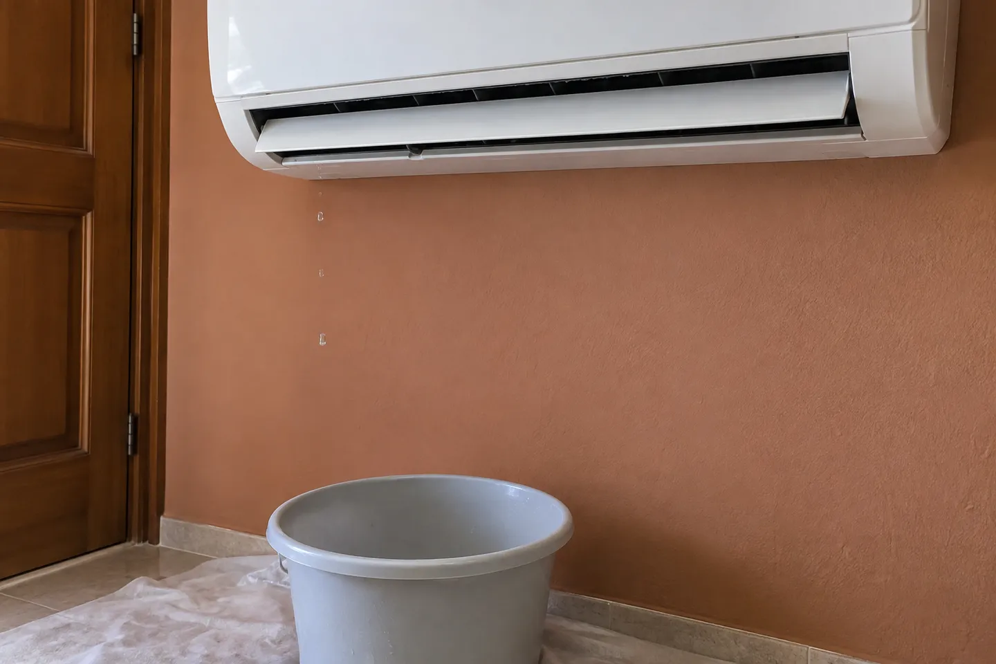Gotas de agua bajo un split interior y recipiente para proteger el suelo